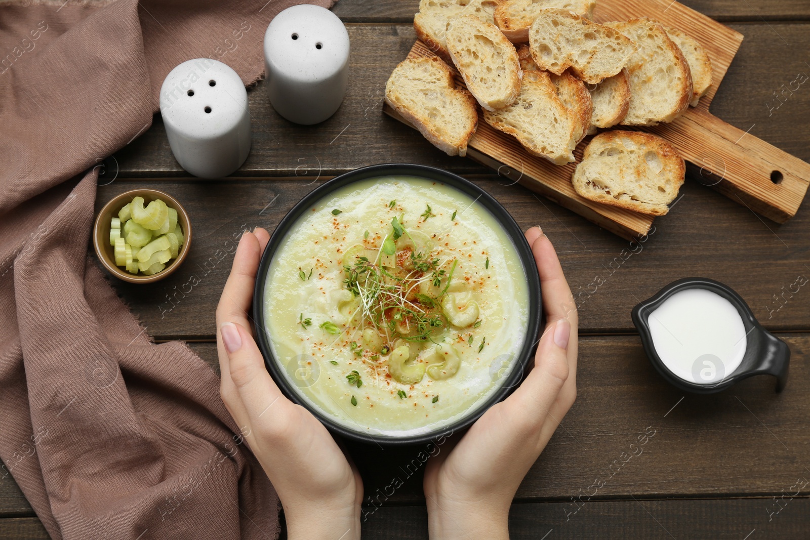 Photo of Woman with bowl of delicious celery soup on wooden table, top view