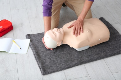Photo of Man practicing first aid on mannequin  indoors, closeup