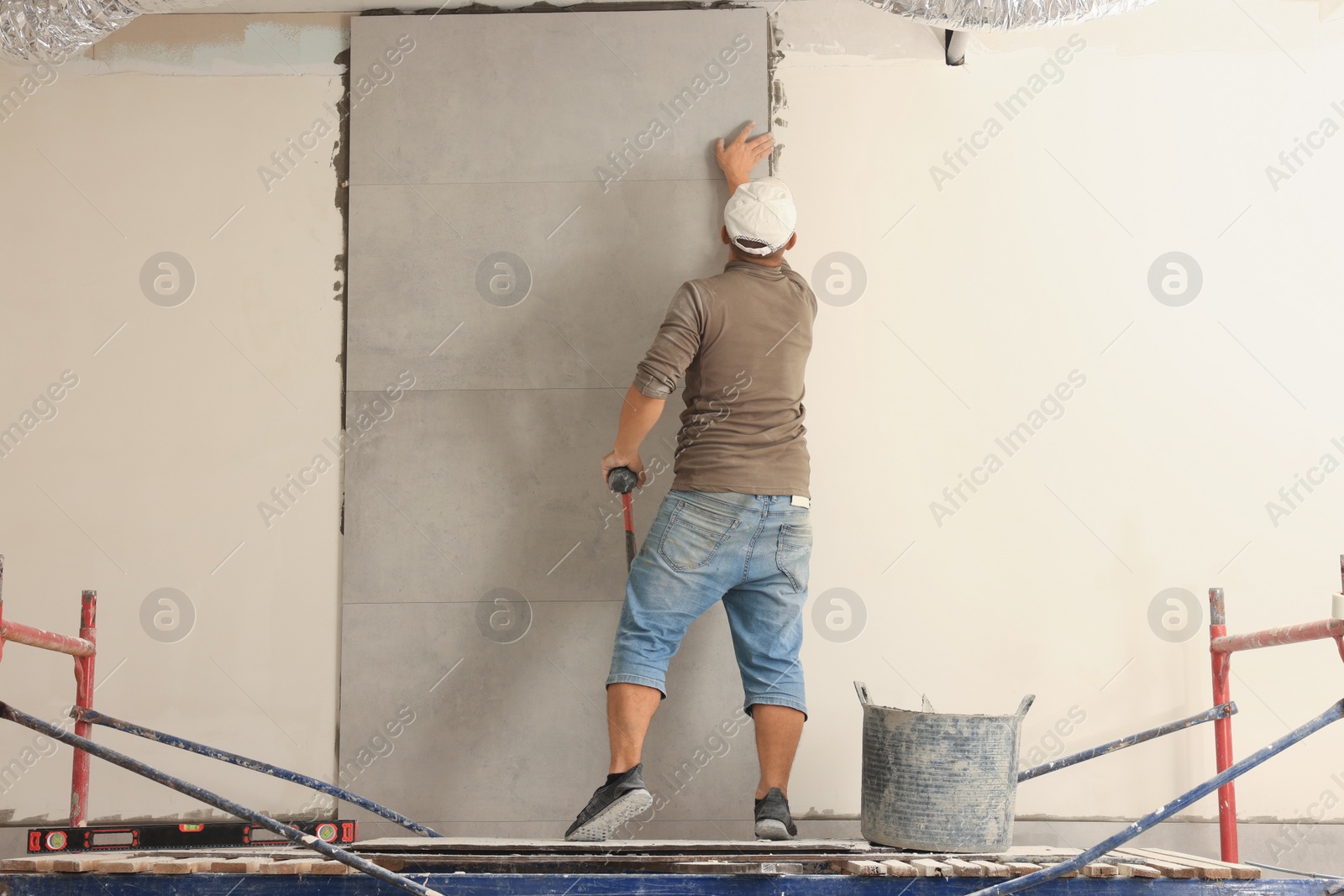 Photo of Worker installing tile on wall indoors, back view