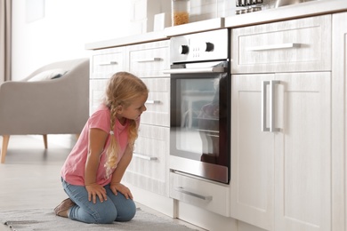 Photo of Little girl sitting near oven in kitchen