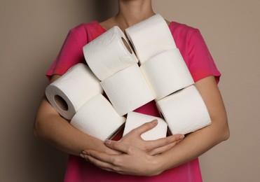 Woman with heap of toilet paper rolls on beige background, closeup