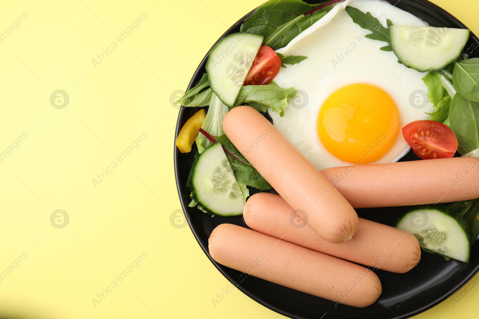 Photo of Delicious breakfast with boiled sausages and fried egg on yellow background, top view. Space for text