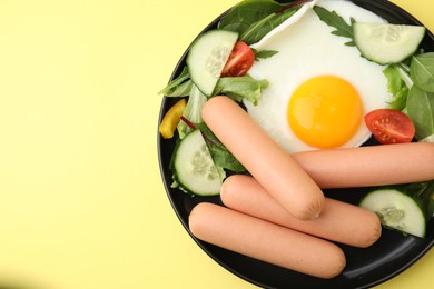 Photo of Delicious breakfast with boiled sausages and fried egg on yellow background, top view. Space for text