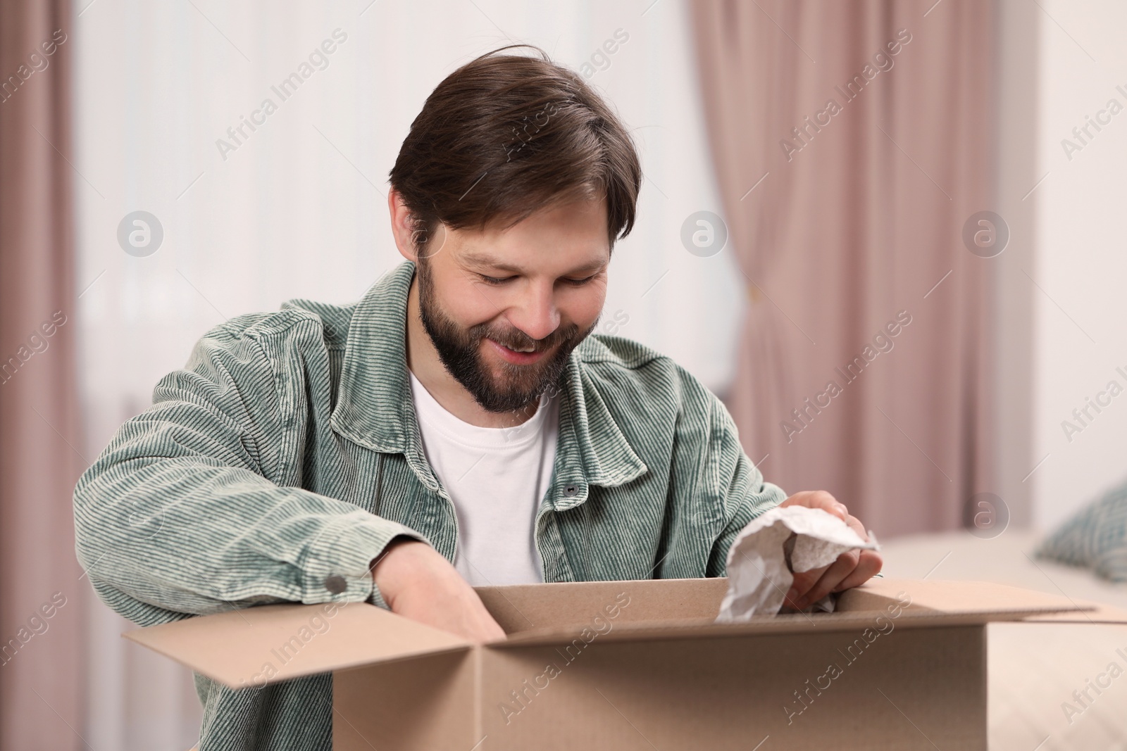 Photo of Happy man opening parcel at home. Internet shopping