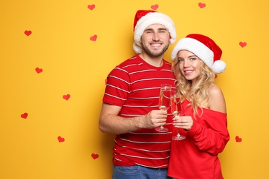 Photo of Young couple in Santa hats with glasses of champagne on color background. Christmas celebration