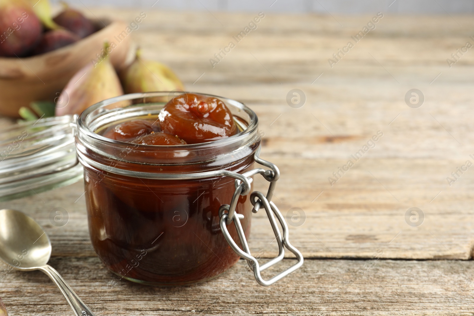 Photo of Jar of tasty sweet fig jam on wooden table. Space for text