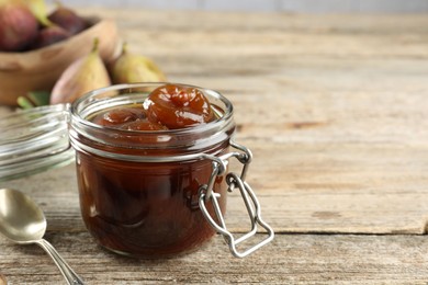 Photo of Jar of tasty sweet fig jam on wooden table. Space for text