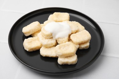 Photo of Plate of tasty lazy dumplings with sour cream on white tiled table