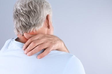 Photo of Senior man scratching neck on grey background, space for text. Allergy symptom