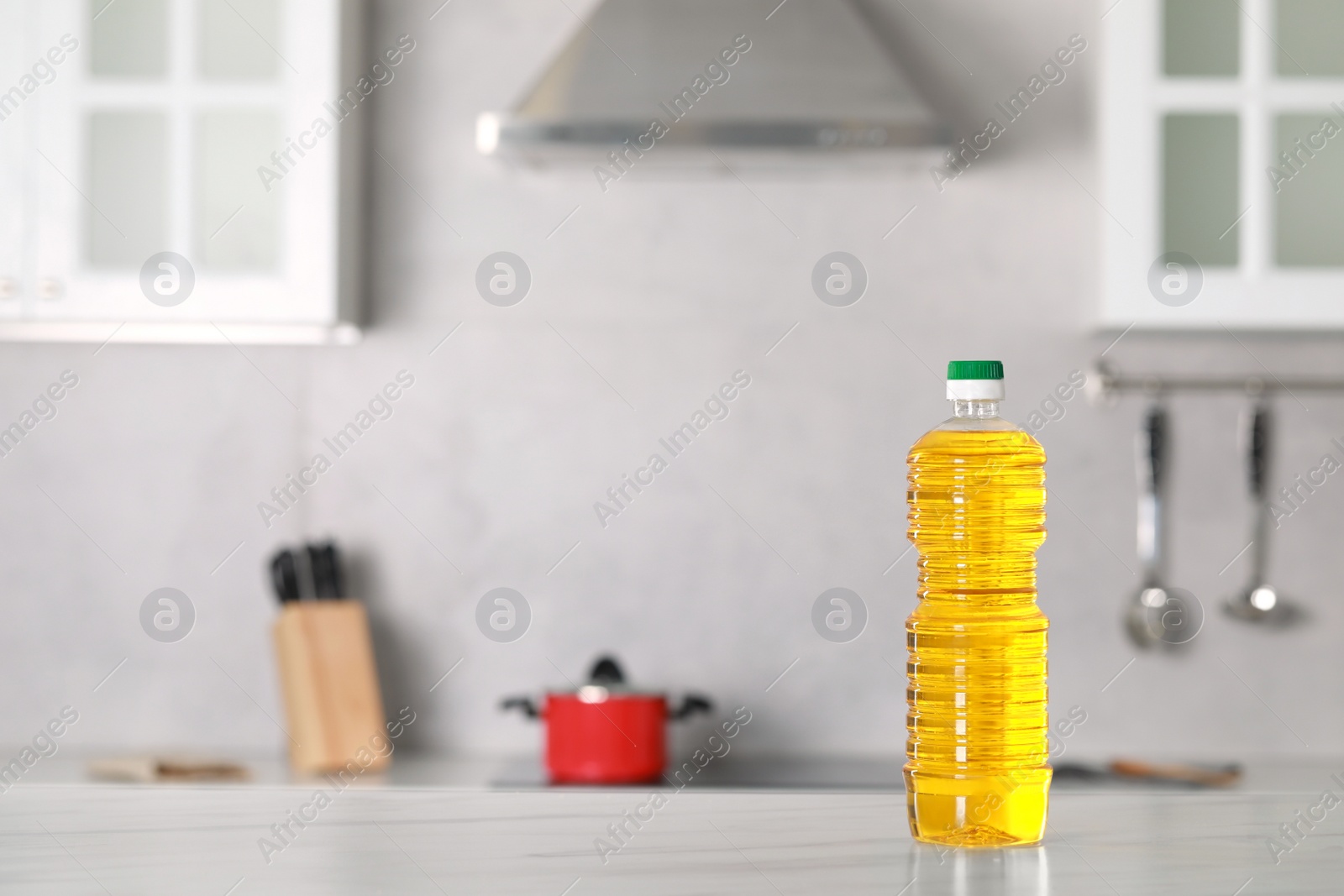 Photo of Bottle of cooking oil on white marble table in kitchen. Space for text