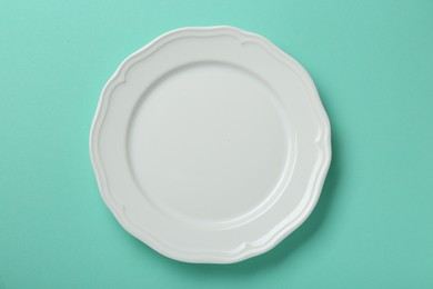 Photo of Empty white ceramic plate on turquoise background, top view