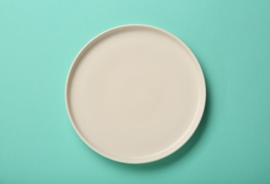 Empty ceramic plate on turquoise background, top view