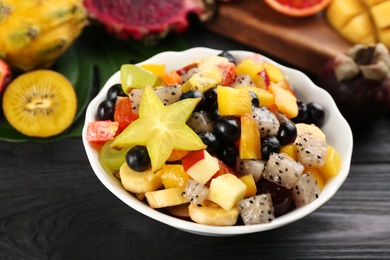 Delicious exotic fruit salad on black wooden table, closeup