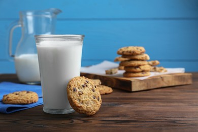 Photo of Delicious chocolate chip cookies and glass of milk on wooden table, space for text