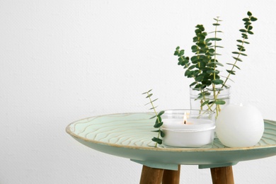 Photo of Composition with burning aromatic candles and eucalyptus on table near white wall. Space for text