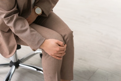 Photo of Young woman suffering from leg pain in office, closeup