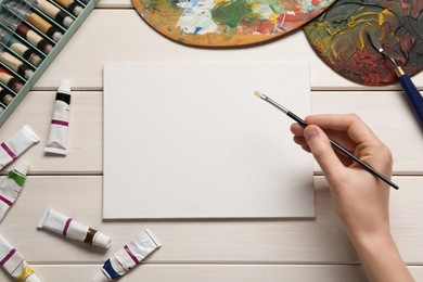 Photo of Man with brush and blank canvas at white wooden table, top view