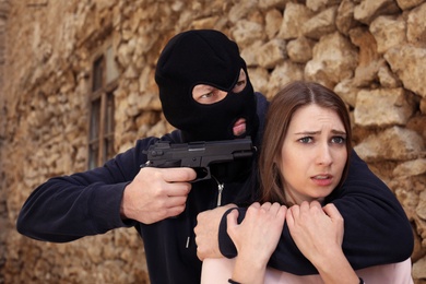 Photo of Masked man with gun holding woman hostage  outdoors. Criminal offence