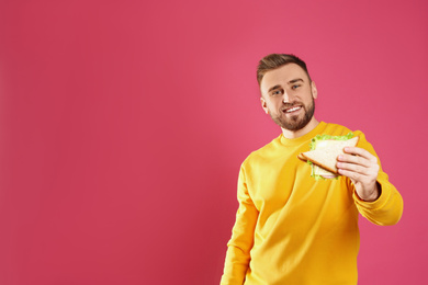 Photo of Young man with tasty sandwich on pink background. Space for text