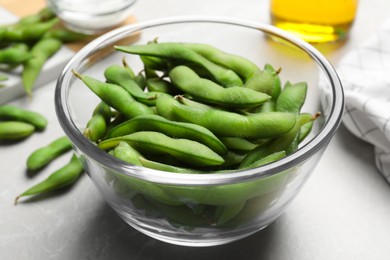Photo of Bowl with green edamame beans in pods on light grey table, closeup