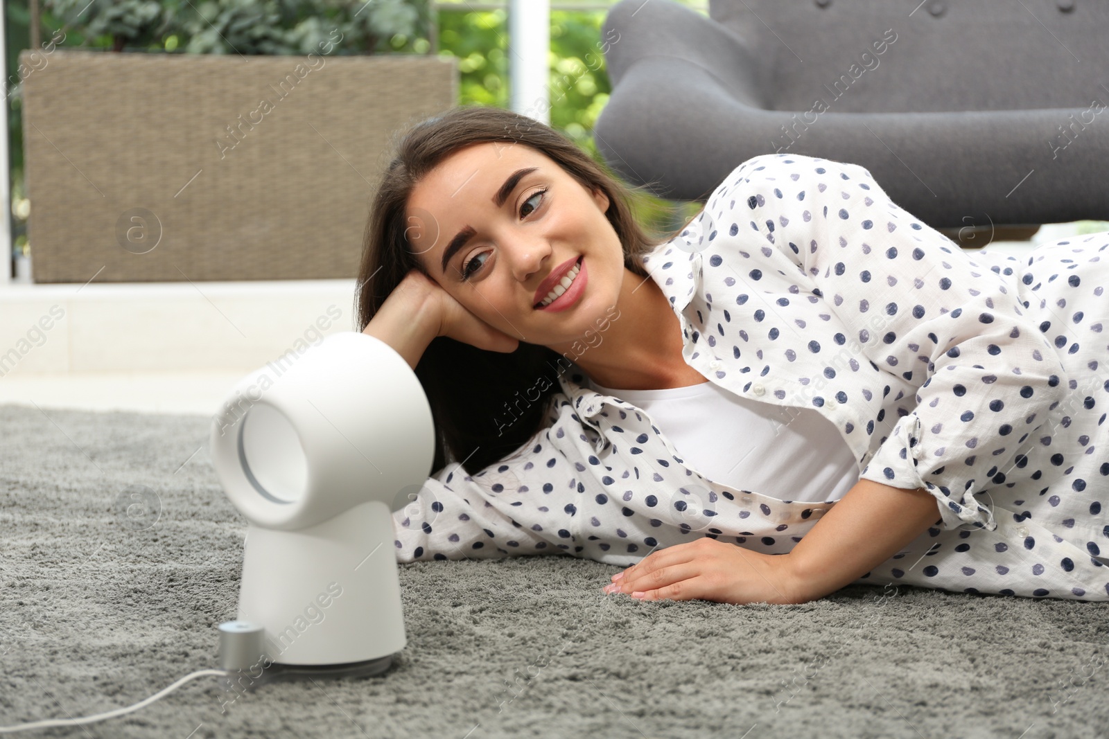 Photo of Woman enjoying air flow from portable fan at home. Summer heat