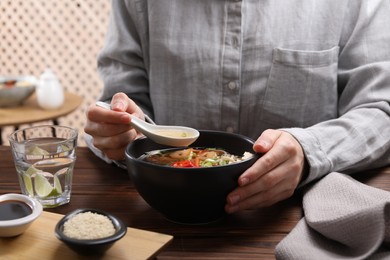 Photo of Woman eating delicious ramen with spoon at wooden table, closeup. Noodle soup