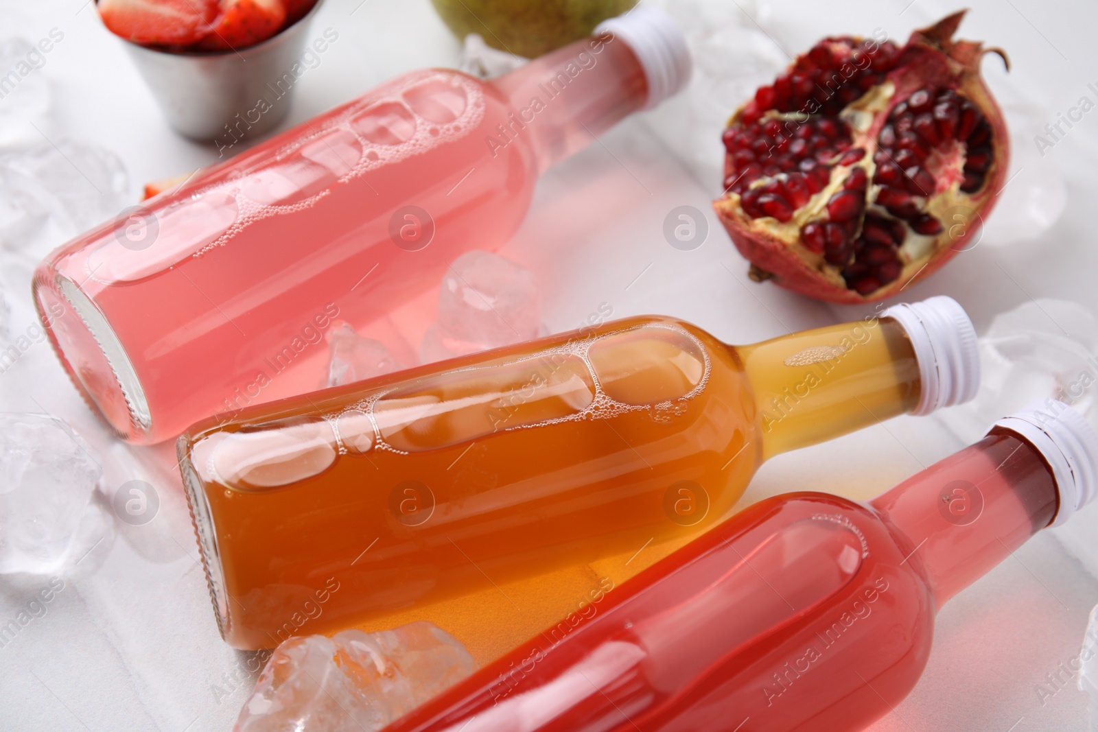 Photo of Tasty kombucha in glass bottles, fresh fruits and ice on white table, closeup