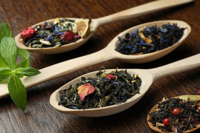 Photo of Spoons with dried herbal tea leaves on wooden table, closeup