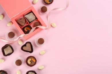Different delicious chocolate candies with box on light pink background, flat lay. Space for text