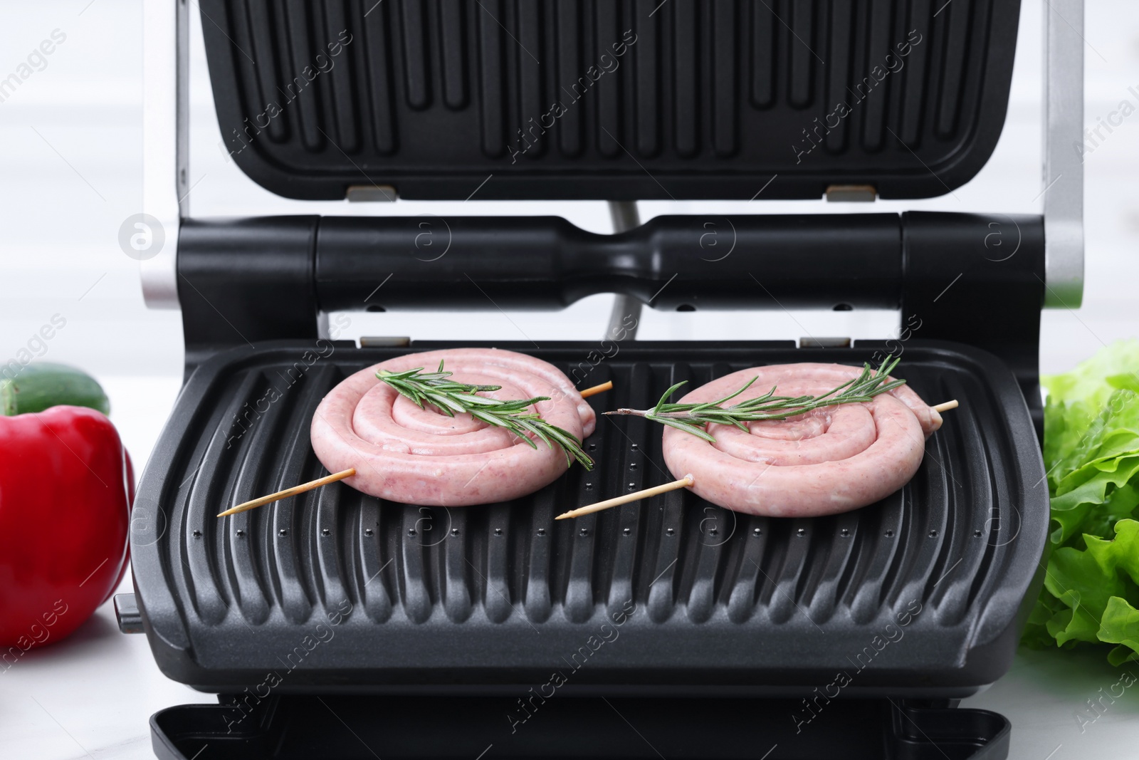 Photo of Electric grill with homemade sausages and rosemary on table, closeup