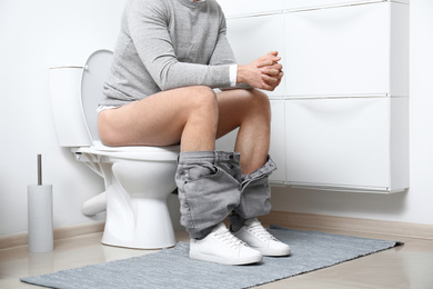 Photo of Man sitting on toilet bowl in bathroom, closeup