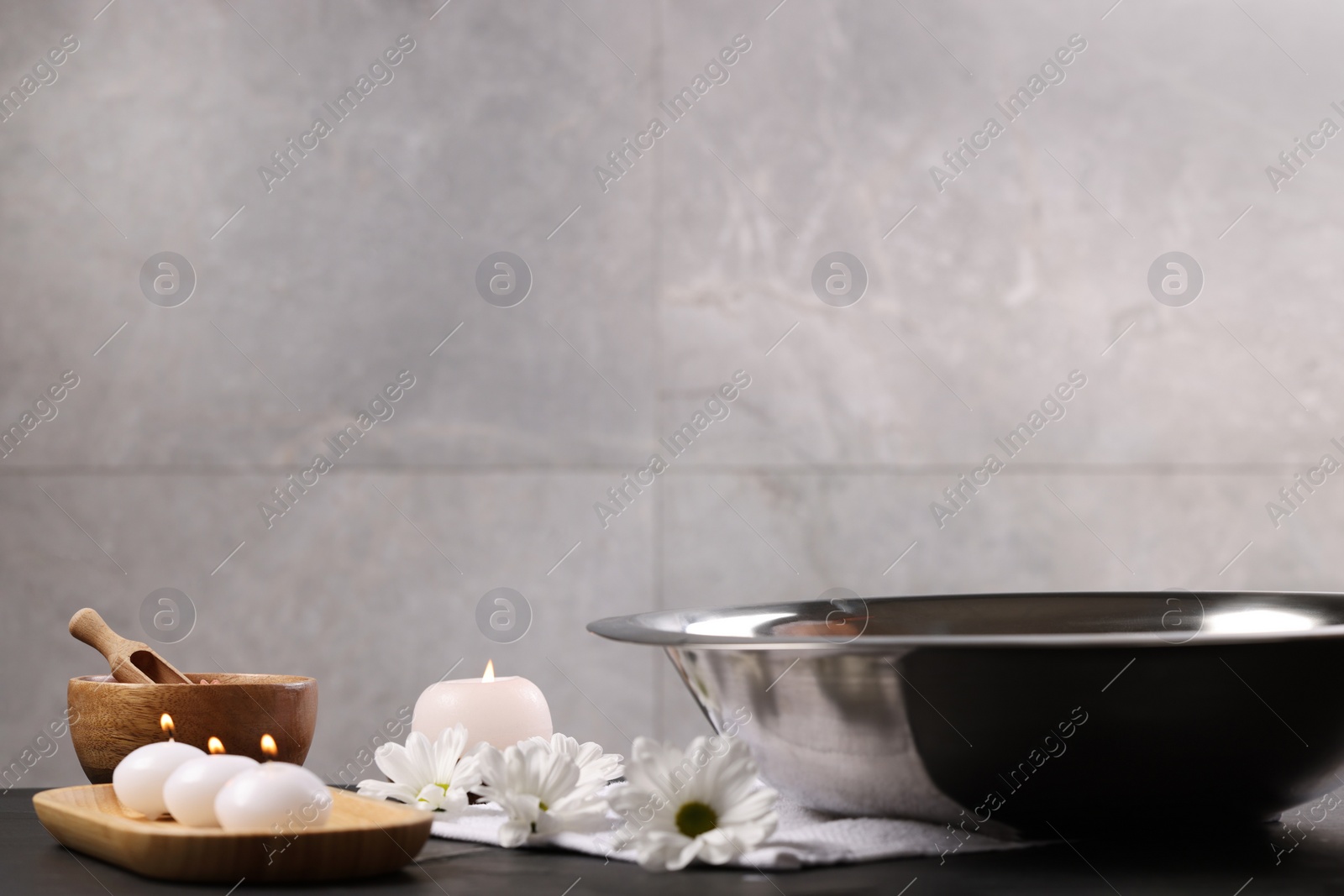 Photo of Bowl of water, flowers, burning candles and sea salt on dark table. Pedicure procedure