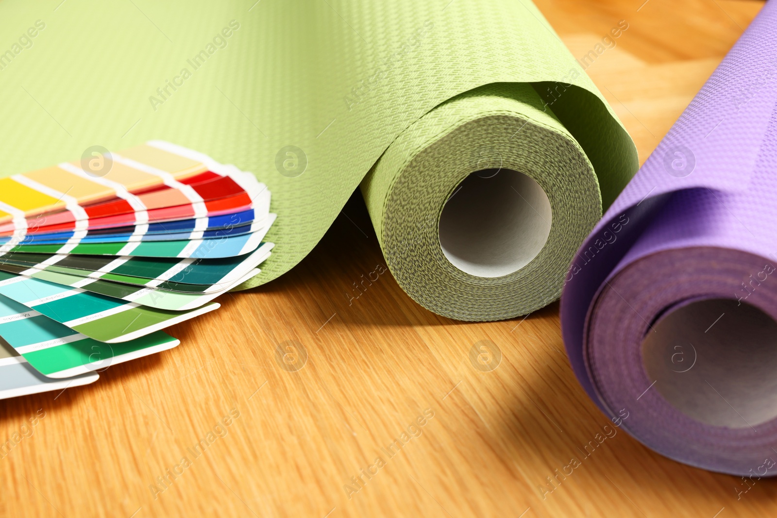 Photo of Different wallpaper rolls and color palette samples on wooden table