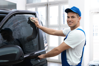 Photo of Worker washing tinted car window in workshop