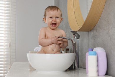 Photo of Cute little baby bathing in sink indoors