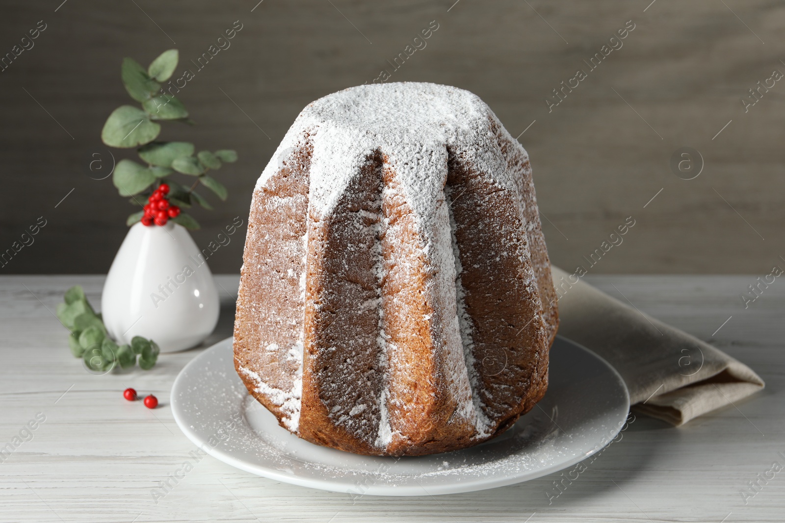 Photo of Delicious Pandoro cake decorated with powdered sugar on white wooden table. Traditional Italian pastry