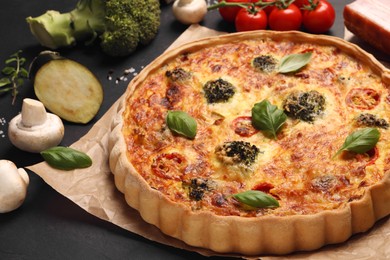 Photo of Delicious homemade vegetable quiche and different vegetables on black table