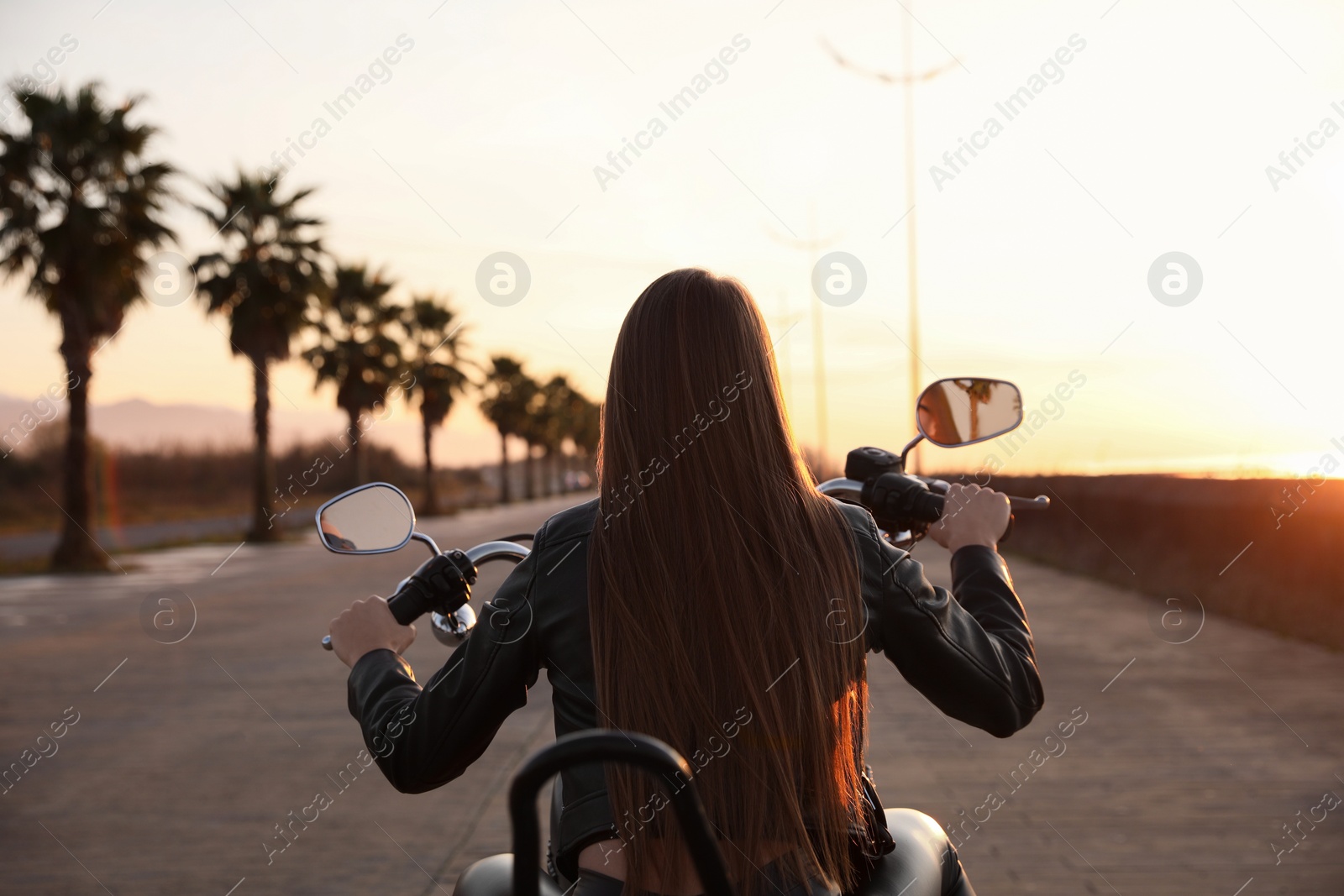 Photo of Woman riding motorcycle at sunset, back view