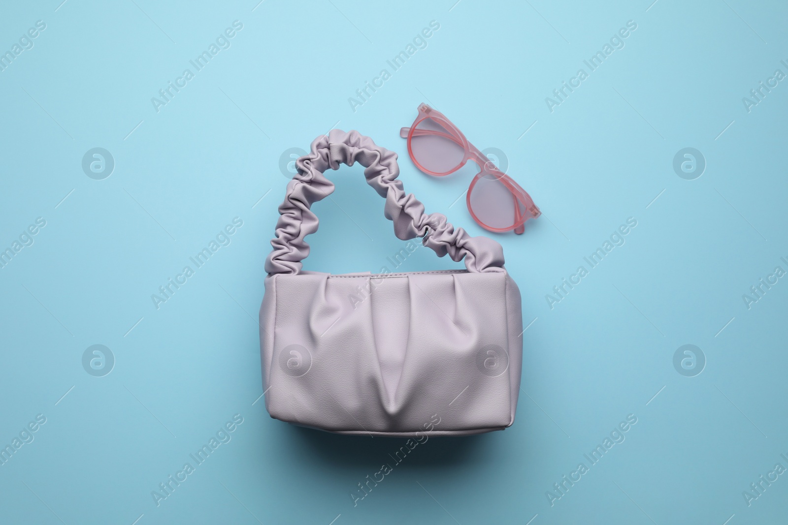 Photo of Stylish woman's bag and sunglasses on light blue background, flat lay