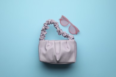 Stylish woman's bag and sunglasses on light blue background, flat lay