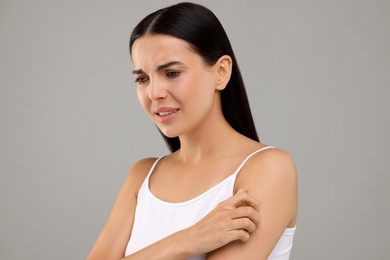 Photo of Suffering from allergy. Young woman scratching her arm on light grey background