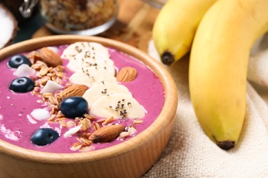 Photo of Delicious acai smoothie with granola and almonds in dessert bowl on table, closeup