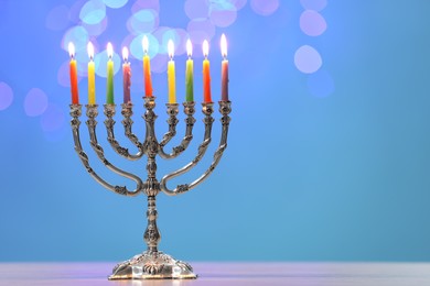 Photo of Hanukkah celebration. Menorah with burning candles on table against blurred lights, space for text