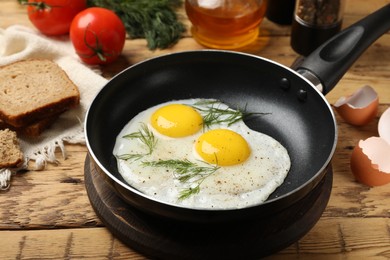 Photo of Frying pan with tasty cooked eggs, dill and other products on wooden table