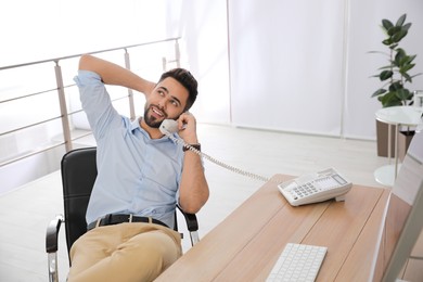 Photo of Relaxed businessman talking on phone in office chair at workplace
