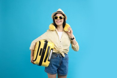 Photo of Happy female tourist with suitcase and travel pillow on light blue background