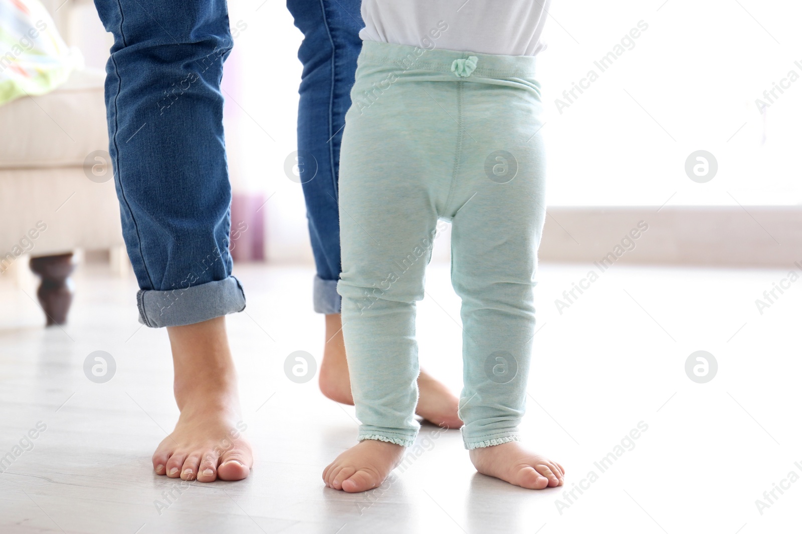 Photo of Baby doing first steps with mother's help, closeup of legs