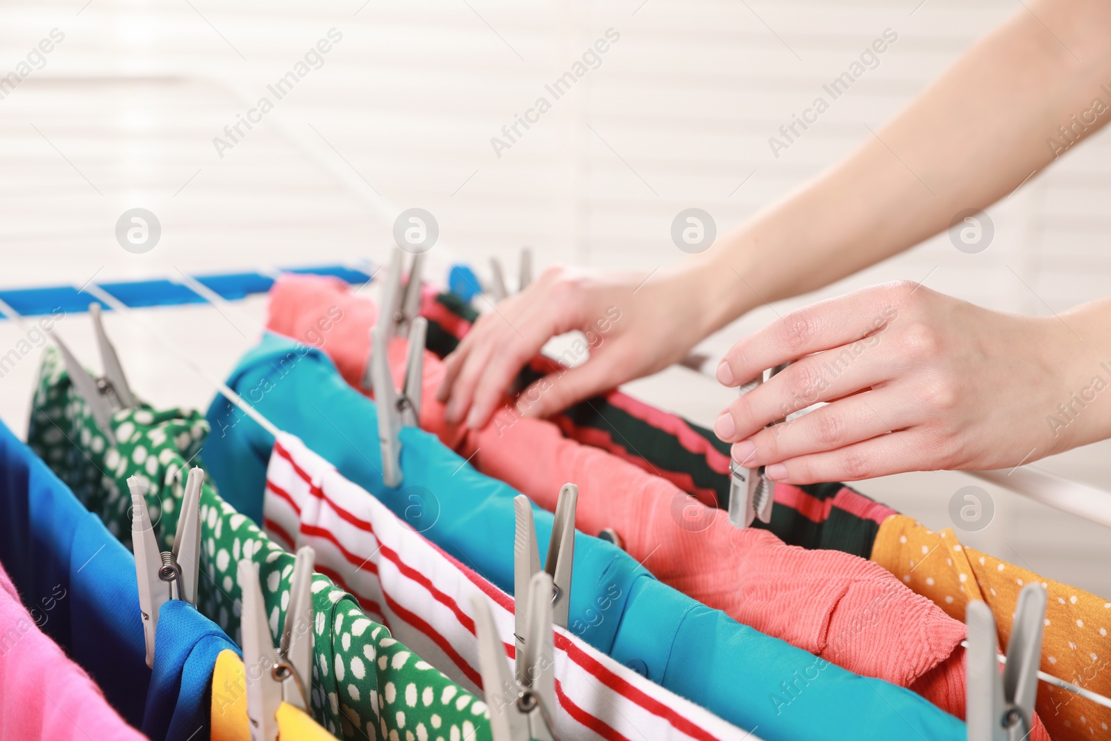 Photo of Woman hanging clean laundry on drying rack indoors, closeup