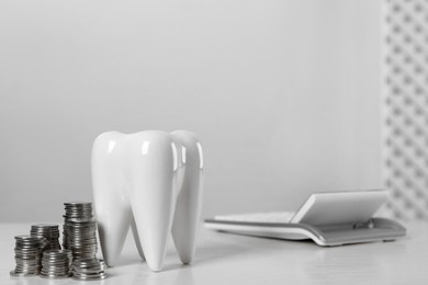Photo of Ceramic model of tooth, coins and calculator on white table, space for text. Expensive treatment