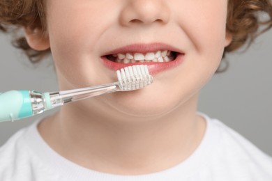 Photo of Cute little boy brushing his teeth with electric toothbrush on light grey background, closeup